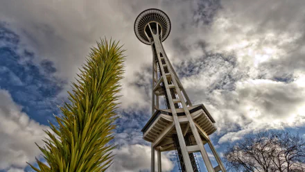HD desktop wallpaper featuring Seattle's iconic man-made Space Needle against a dramatic cloudy sky with green foliage in the foreground.