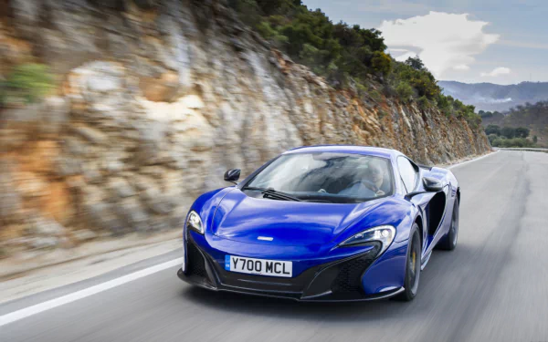 Blue McLaren 650S supercar driving along a winding coastal road — HD PC desktop wallpaper background.