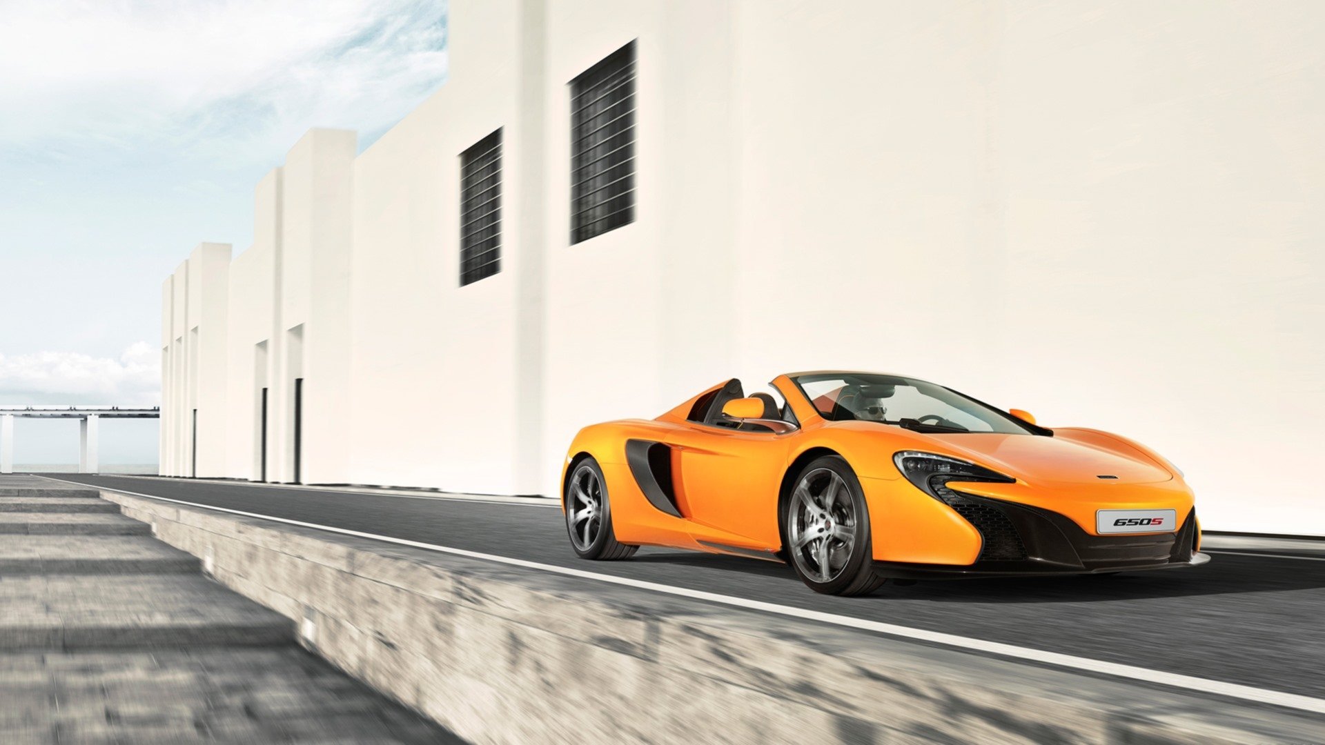 Orange McLaren 650S Spider supercar on a city road beside a white building, HD PC desktop wallpaper background