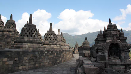 Borobudur Buddhist temple stupas and stone terraces against a blue sky and distant mountains — HD PC desktop wallpaper background.