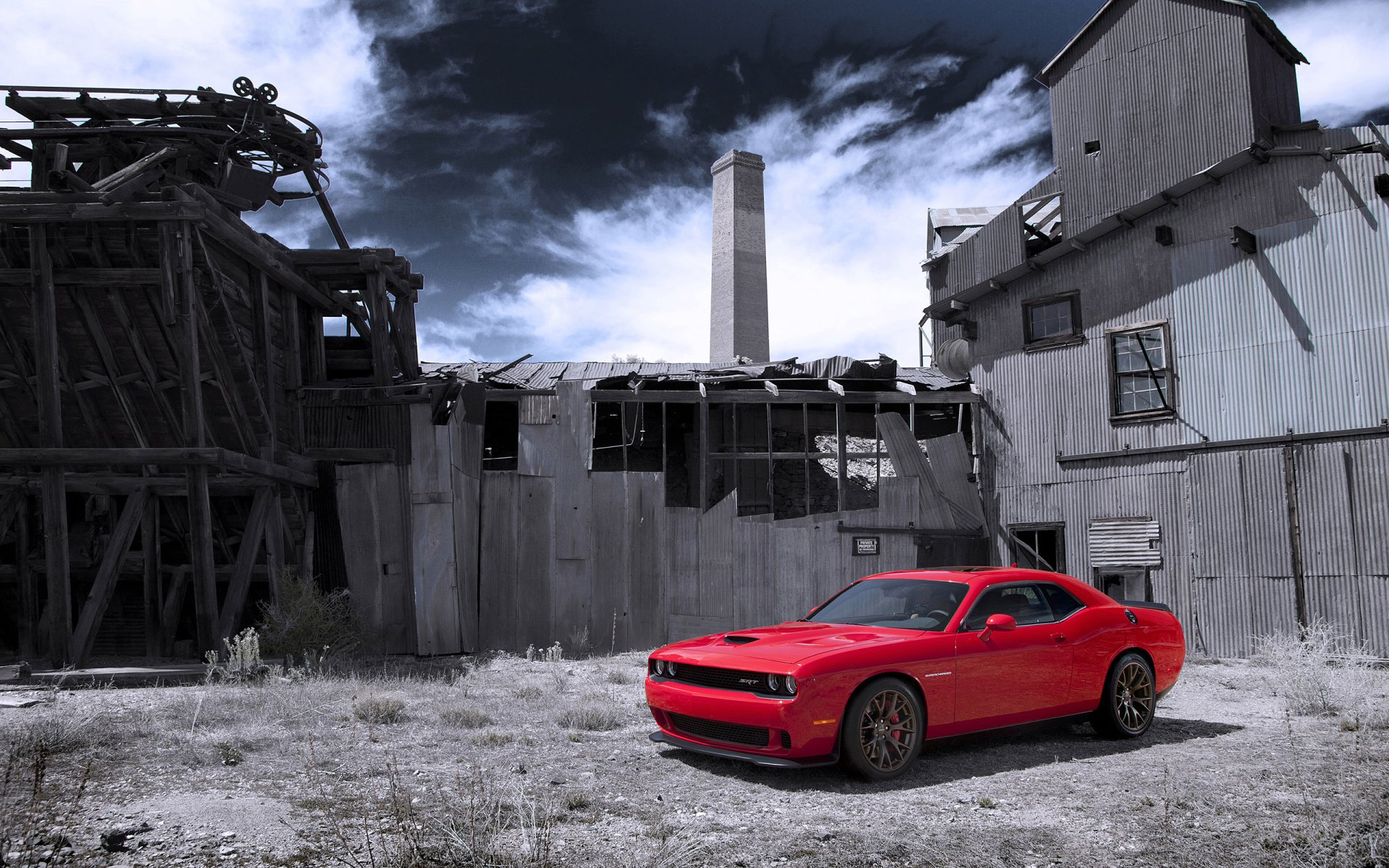 HD desktop wallpaper featuring a red Dodge Challenger SRT Hellcat muscle car parked in front of a rundown industrial building under a cloudy sky.