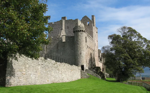 A clear view of Craigmillar Castle, a man-made stone fortress, set against a bright blue sky with trees and green grass in the foreground, captured in HD for a desktop wallpaper.