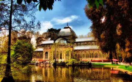 HD desktop wallpaper showcasing the man-made Palacio de Cristal, surrounded by trees and reflected in a tranquil pond under a vibrant sky.