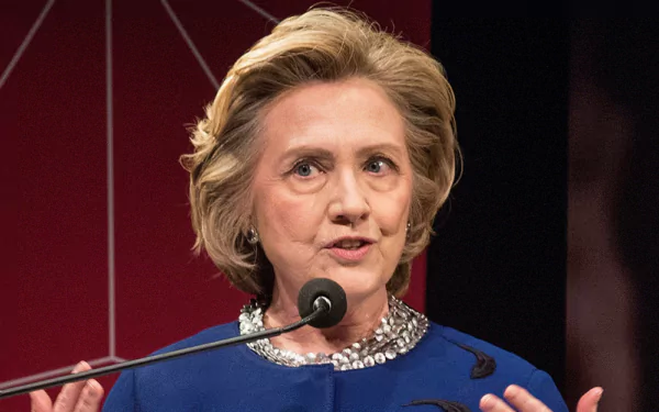 HD desktop wallpaper of a woman speaking at a podium, dressed in blue with a microphone in front.