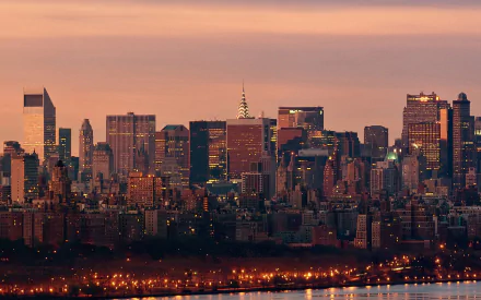 HD desktop wallpaper showcasing the illuminated skyline of New York City at sunset, highlighting its iconic man-made architectural structures.