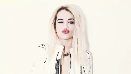 HD wallpaper featuring Rita Ora striking a playful pose, winking and puckering her lips, set against a clean, light background.