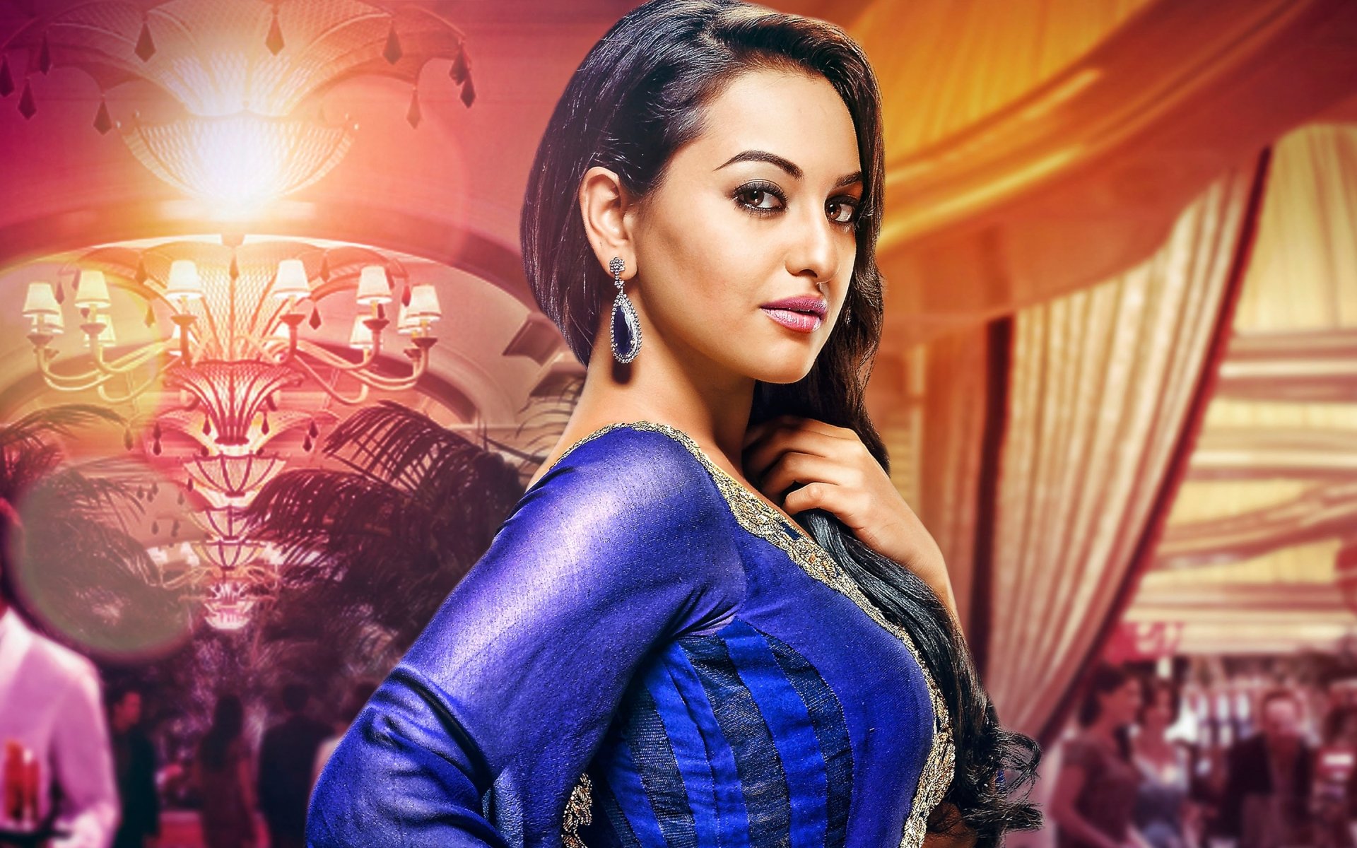 A vibrant HD desktop wallpaper and background featuring Indian celebrity Sonakshi Sinha in a blue traditional outfit, standing in a beautifully decorated, warmly lit interior.