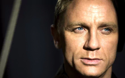 Close-up HD desktop wallpaper of English actor Daniel Craig with sharp facial features and intense blue eyes against a dark background.