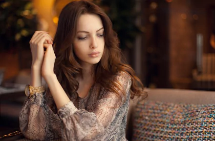 HD desktop wallpaper featuring model Bianca Dragusanu, a woman with long brown hair, seated thoughtfully in a warmly lit indoor setting.