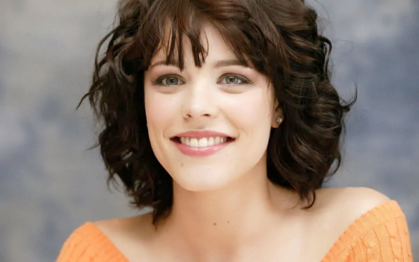 HD desktop wallpaper featuring a portrait of a woman with a cheerful smile, wearing an orange top with curly hair.