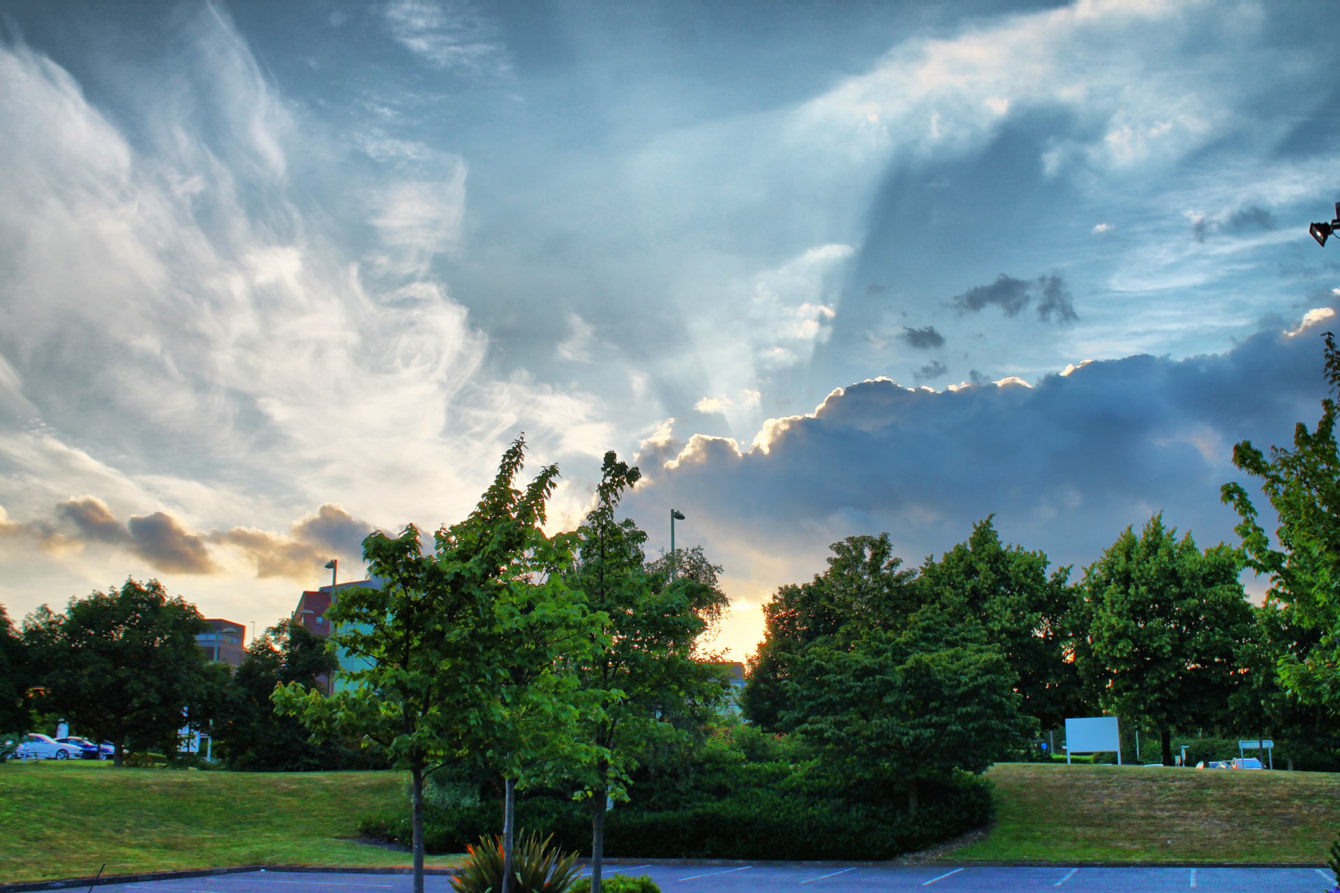 A vibrant 4K Ultra HD desktop wallpaper showcasing a serene green park under a dramatic sky filled with clouds and soft sunlight.