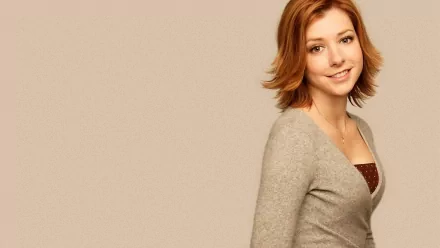 HD desktop wallpaper featuring celebrity Alyson Hannigan with a warm smile, wearing a light grey cardigan against a beige background.