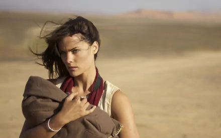 HD desktop wallpaper featuring American actress and celebrity Jaimie Alexander in a desert setting, holding a brown garment with wind blowing through her hair.
