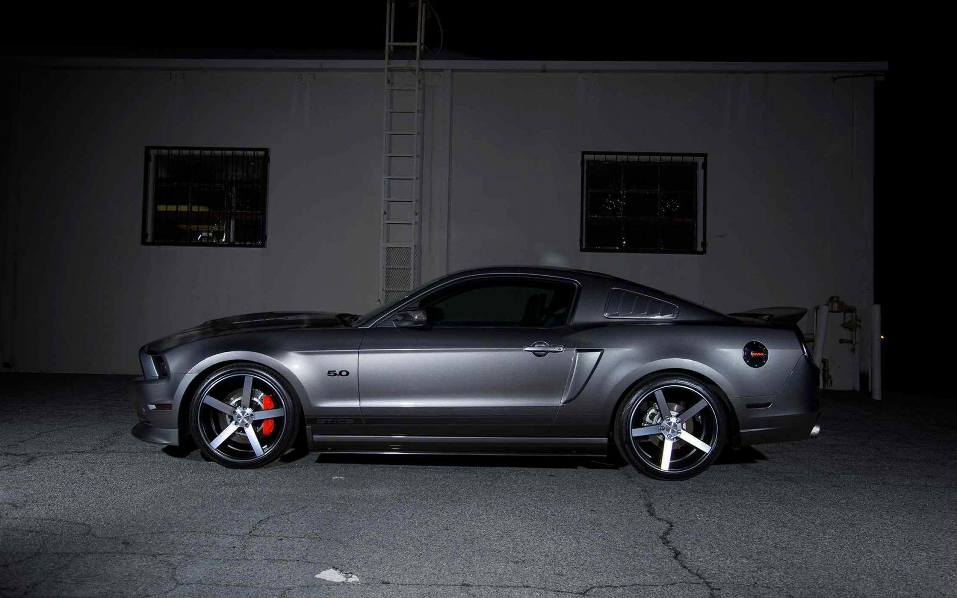 A sleek gray Ford Mustang parked against a dark background, showcasing its stylish design and performance features. This image serves as a striking HD desktop wallpaper.
