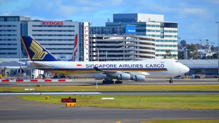A Singapore Airlines Cargo Boeing 747 taxis at Sydney Airport, surrounded by modern buildings, showcasing the dynamic air transport scene. High-definition desktop wallpaper.
