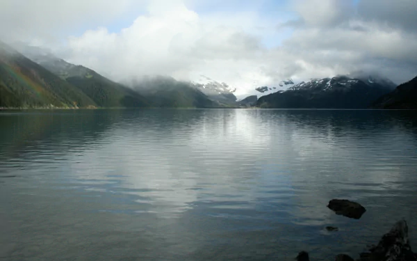 Calm waters of Garibaldi Lake reflect snowy mountains under a cloudy sky, showcasing serene nature in this HD PC desktop wallpaper.