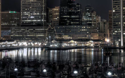 Nighttime view of Baltimore’s cityscape with illuminated buildings, a calm river, and boats docked along the waterfront, captured in HD for a desktop wallpaper.