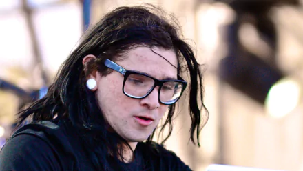 A close-up of Skrillex performing, showcasing his signature style with long hair and glasses. This image serves as a vibrant HD wallpaper for music enthusiasts.