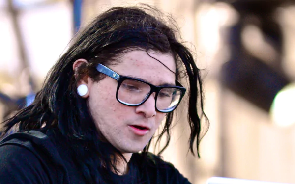 A close-up of Skrillex performing, showcasing his signature style with long hair and glasses. This image serves as a vibrant HD wallpaper for music enthusiasts.
