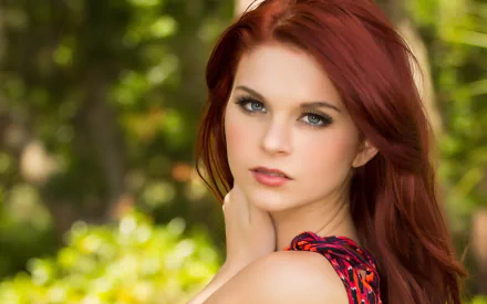 HD desktop wallpaper featuring a portrait of a woman with striking red hair and green eyes, set against a softly blurred natural background.