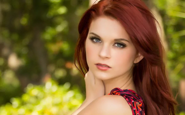 HD desktop wallpaper featuring a portrait of a woman with striking red hair and green eyes, set against a softly blurred natural background.