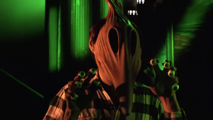 HD PC desktop wallpaper from the movie Beetlejuice: eerie, distorted sandworm-like face, striped suit and eyeball necklace, bathed in green light.