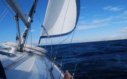 HD PC desktop wallpaper background showing a sailboat vehicle from the deck, white sails billowing over deep blue sea under a clear sky.