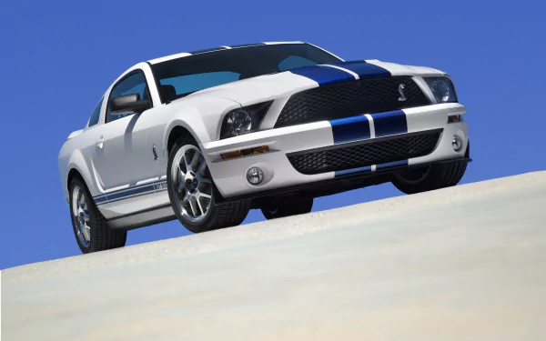Front three-quarter view of a white Ford Mustang Shelby Cobra GT500 with blue racing stripes against a clear blue sky, HD PC desktop wallpaper.