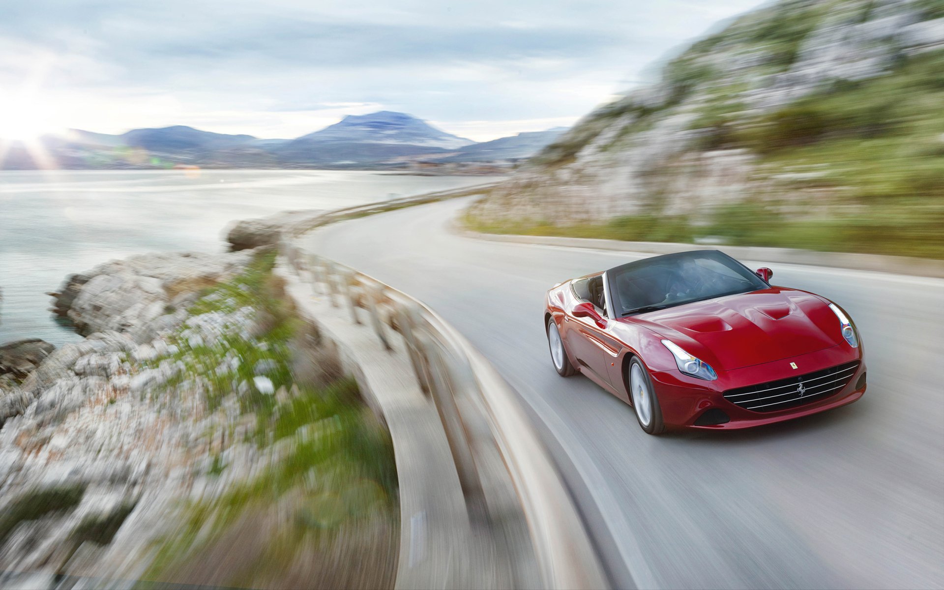 Red Ferrari California T speeds along a coastal road, captured in this HD PC desktop wallpaper showcasing the sleek vehicle against a scenic mountainous backdrop.