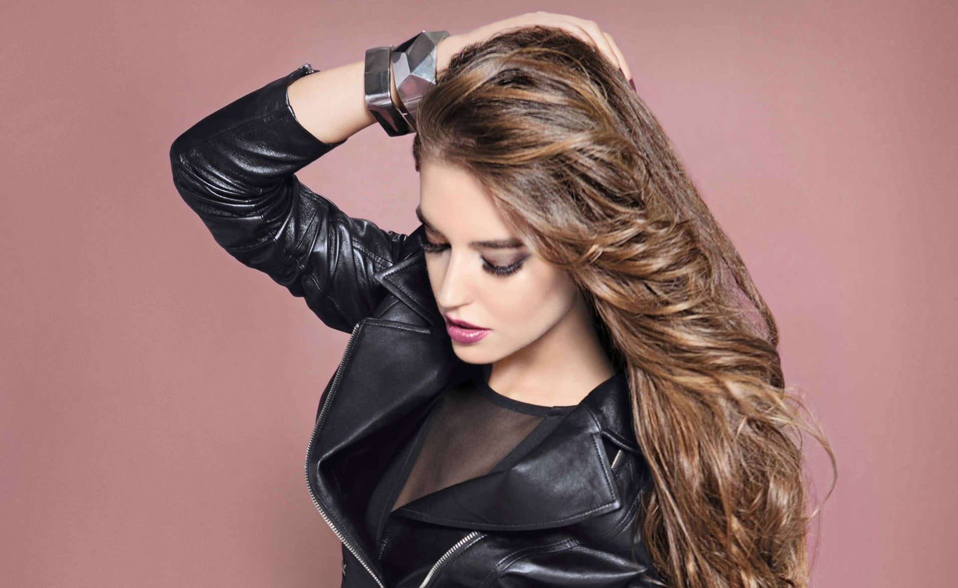 HD desktop wallpaper featuring Spanish woman Clara Alonso with long flowing hair, wearing a black leather jacket against a muted pink background.