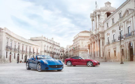 HD PC desktop wallpaper featuring two Ferrari California T vehicles, one blue and one red, parked in a historic European square with classic architecture.