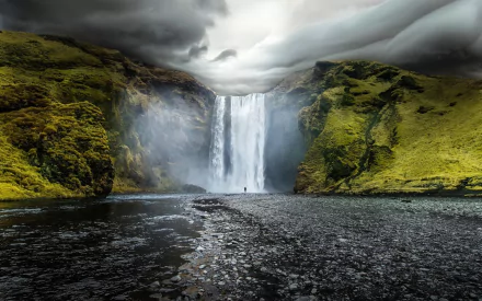 A stunning view of Skógafoss waterfall in Iceland, framed by lush green hills and dramatic clouds, capturing the beauty of nature in a captivating HD wallpaper.
