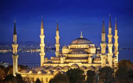 A stunning HD wallpaper featuring the Sultan Ahmed Mosque illuminated at dusk, showcasing its magnificent domes and towering minarets against a deep blue sky.