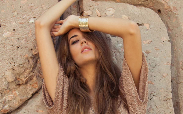 HD desktop wallpaper featuring Spanish woman Clara Alonso posing with arms raised against a textured stone background.
