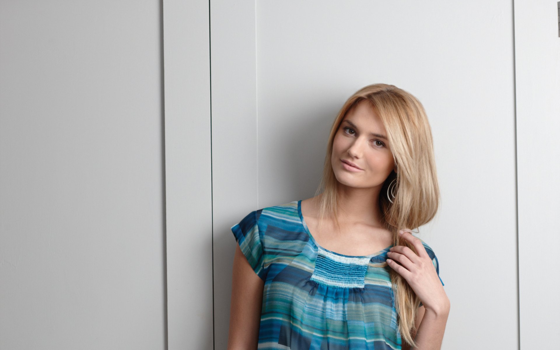 HD PC desktop wallpaper featuring French model Nadege Dabrowski posing against a light grey wall, wearing a blue patterned top.