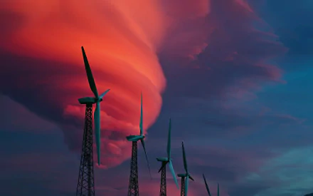 A stunning HD wallpaper featuring wind turbines silhouetted against a dramatic sky, illuminated by vibrant pink and orange clouds at sunset.