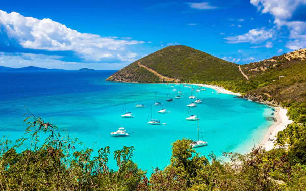 Serene tropical coastline in the Virgin Islands, featuring a vibrant lagoon with boats anchored in crystal-clear waters and lush greenery against a backdrop of rolling hills.