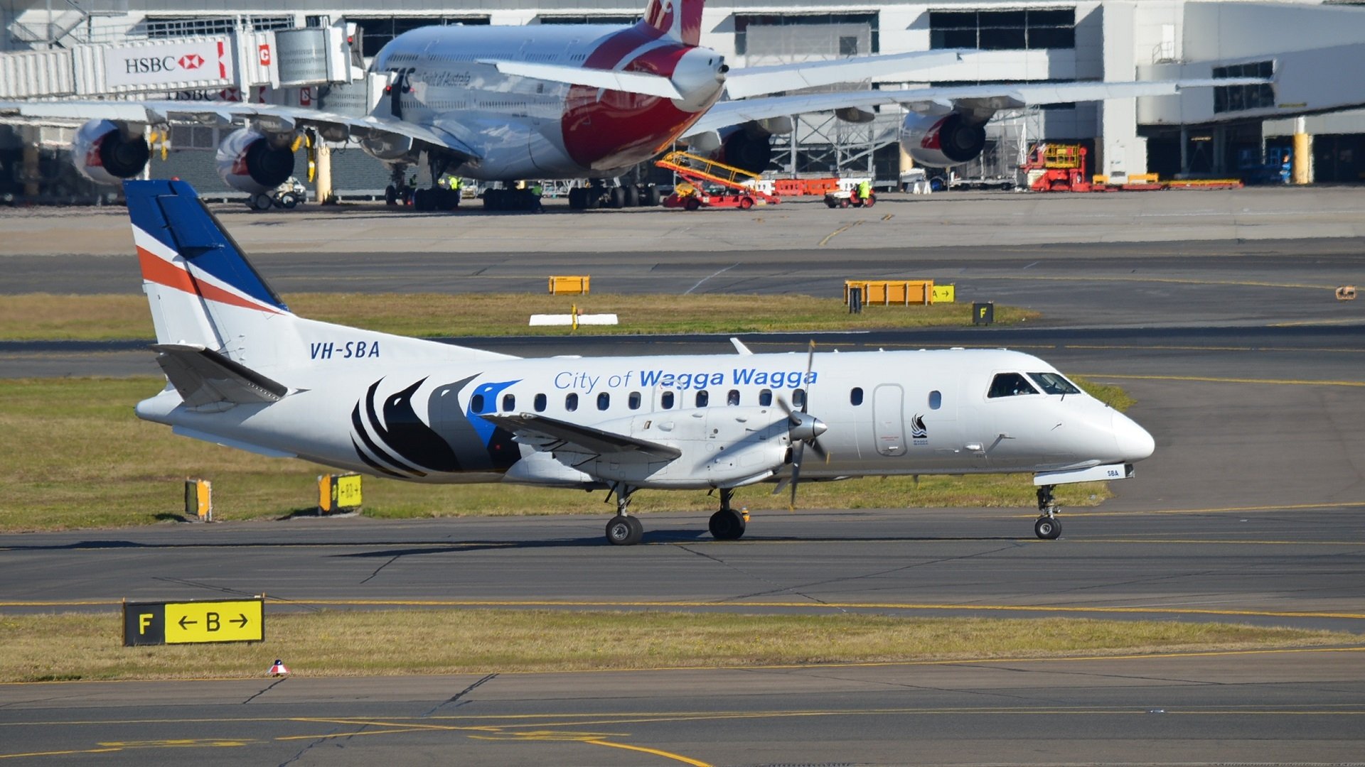 Saab 340B aircraft of City of Wagga Wagga taxiing at Sydney airport with other airplanes and terminal in the background, shown in a sharp HD desktop wallpaper.