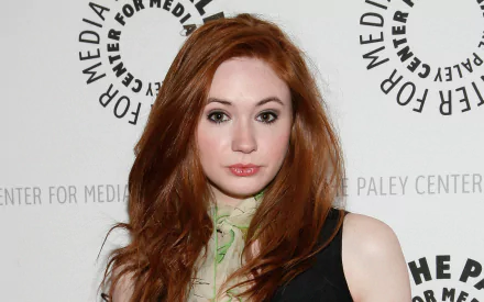 HD desktop wallpaper close-up of a red‑haired woman in a black dress and green scarf posing before a media step-and-repeat backdrop.