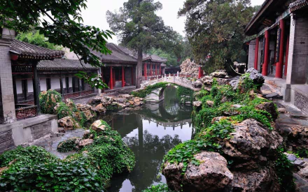 A serene view of a traditional Chinese garden in Beijing, featuring lush greenery, a tranquil pond, and a picturesque bridge, perfect for desktop wallpaper.