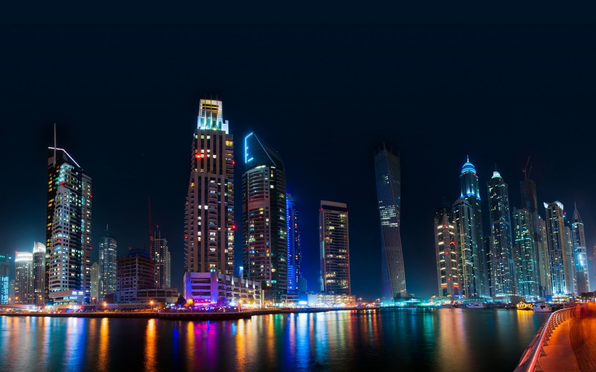 HD PC desktop wallpaper of Dubai’s illuminated skyline at night, showcasing modern man-made skyscrapers reflecting on the water.