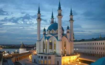 Night view of Qolşärif Mosque with illuminated minarets in Kazan, Russia, set against a cloudy sky and cityscape, captured in high-definition.