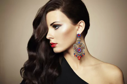 HD portrait of a brunette woman with long hair and striking earrings, captured in a close-up profile shot against a smooth background.