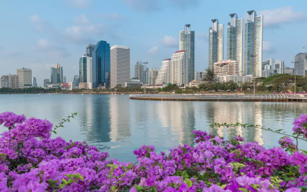 HD desktop wallpaper of Bangkok's man-made skyline along the Chao Phraya River, Thailand, featuring modern high-rise buildings and vibrant purple flowers in the foreground.