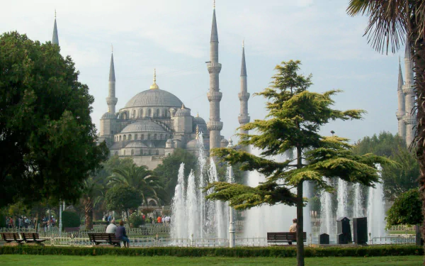 Fountain in front of the Sultan Ahmed Mosque in Istanbul, Turkey, surrounded by trees and greenery under a clear sky.