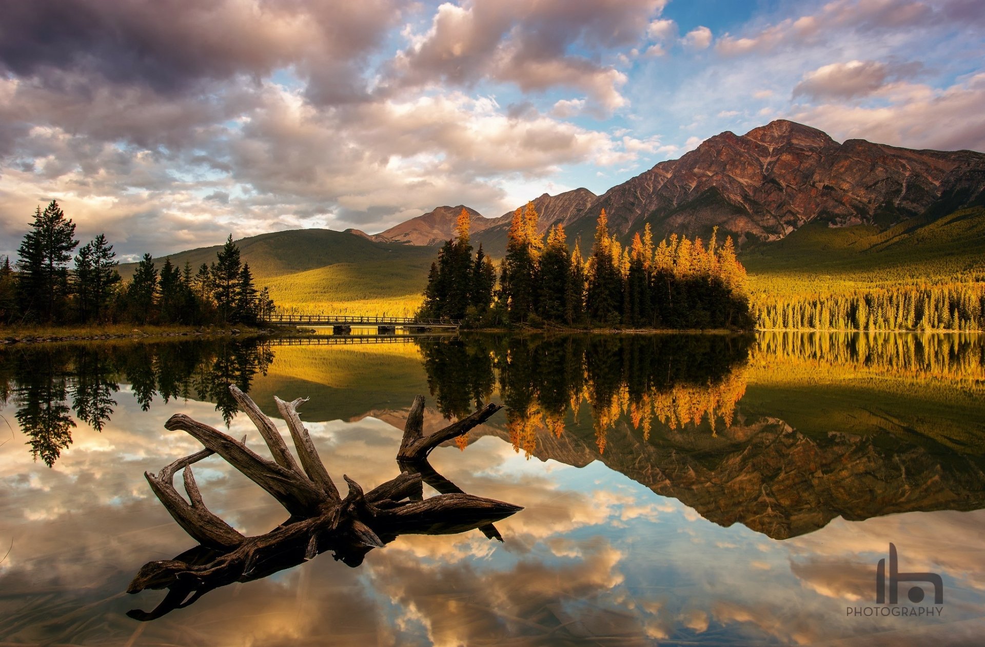 Sunlit mountains and clouds reflect on the calm lake in Jasper National Park, Alberta, Canada, showcasing pristine nature in this HD desktop wallpaper.