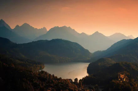 A stunning view of Hohenschwangau Castle nestled in the Bavarian forest, surrounded by majestic mountains and a serene lake, captured during a beautiful sunset.