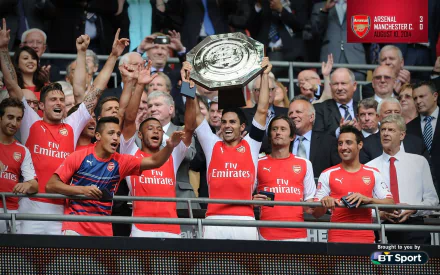 Arsenal F.C. players celebrate a victory, lifting a trophy in front of a cheering crowd. A vibrant HD wallpaper capturing the excitement of sports fandom.