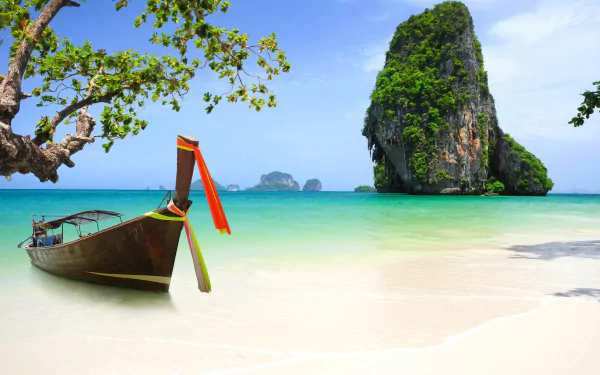 A serene tropical lagoon in Phuket, Thailand, features a traditional boat on sandy shores, surrounded by lush cliffs and clear turquoise waters. A captivating HD desktop wallpaper.
