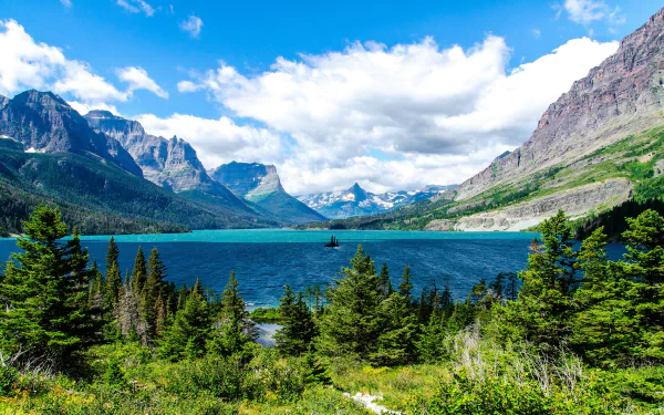Saint Mary Lake panorama: turquoise water, pine-forested shore and jagged mountain peaks beneath a bright sky — 2K Quad HD PC desktop wallpaper and background.